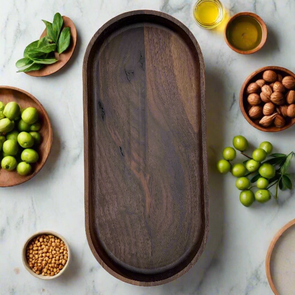 A dark walnut wood serving tray placed on a marble surface, surrounded by various serving bowls and a small pile of walnuts.