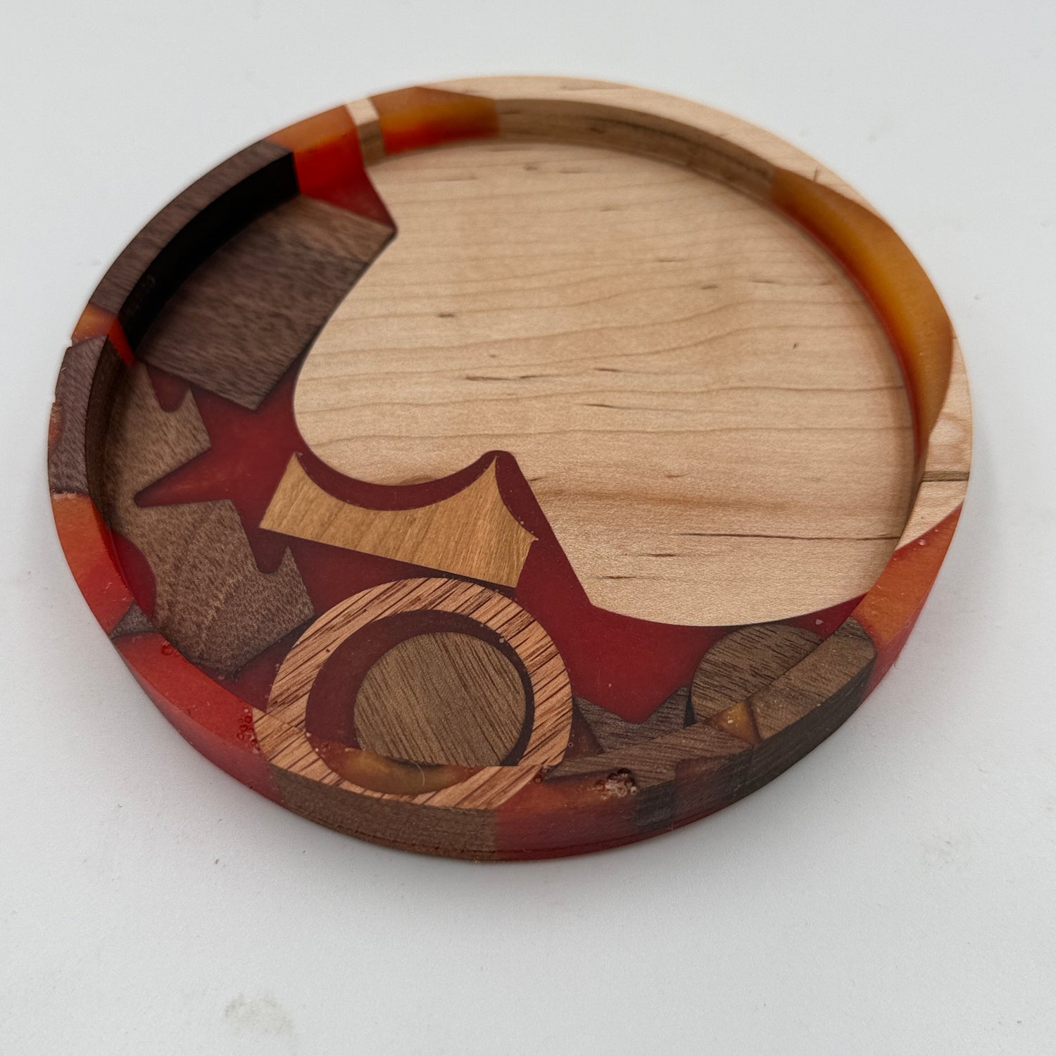 A round wooden coasters or trivets featuring a handcrafted inlay design with star, crescent, and circular motifs in various wood tones and reddish-brown accents, shown on a plain white background.