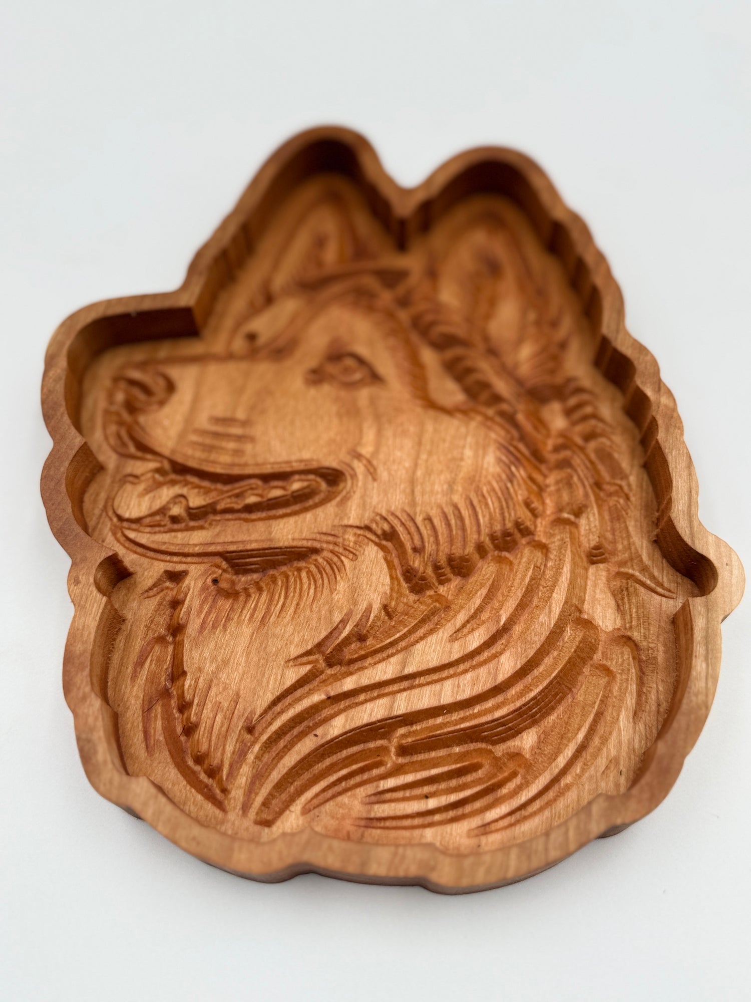 A carved wooden dog head plaque or tray with detailed wood grain and a smooth, slightly polished finish, set against a plain light gray background.