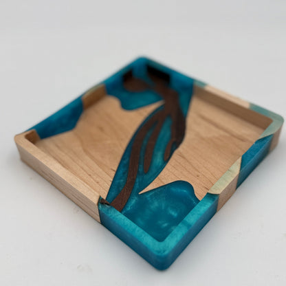A square wooden tray with a natural wood base and vibrant teal blue resin inlay, featuring a dark brown abstract wave-like pattern running down the center.