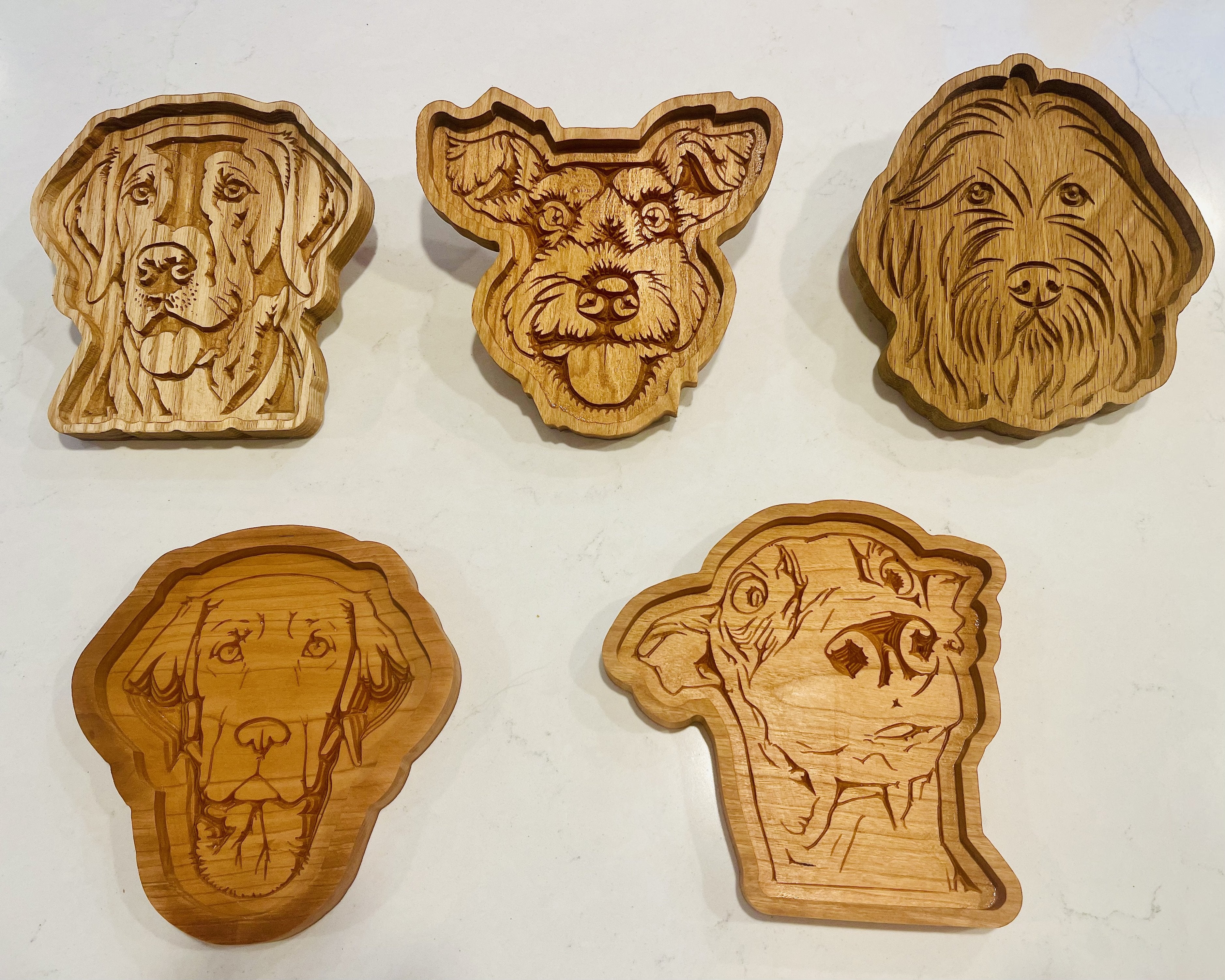 Five hand-carved wooden dog head sculptures in various breeds, displayed on a light off-white background.